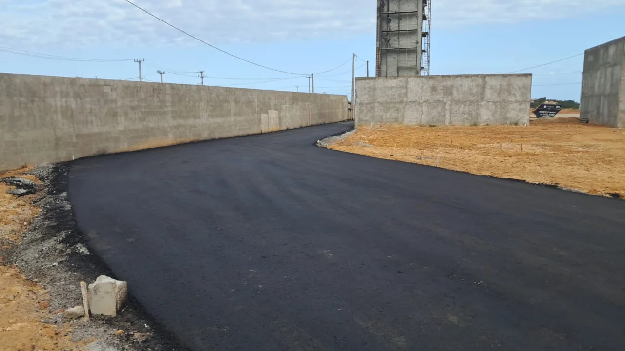 Asfalto concluído na via de acesso à portaria, com a torre do reservatório ao fundo.