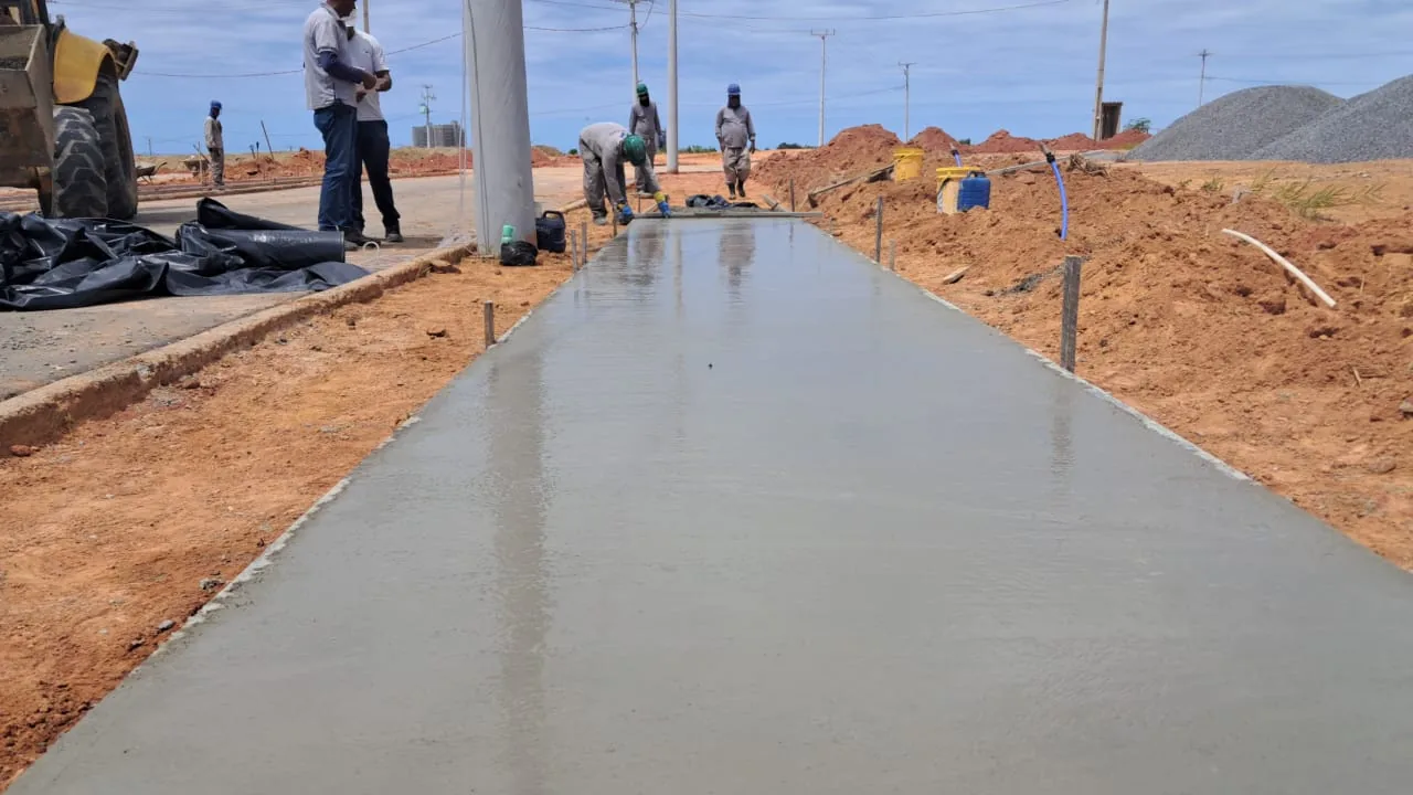 Concretagem de calçada em andamento, com a equipe no acabamento da superfície.